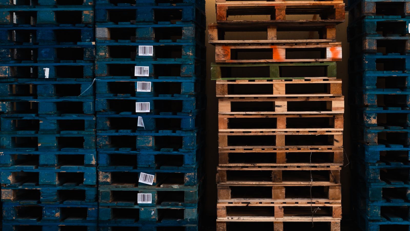 Stacks of blue and natural wood pallets with barcode labels in an industrial storage area.